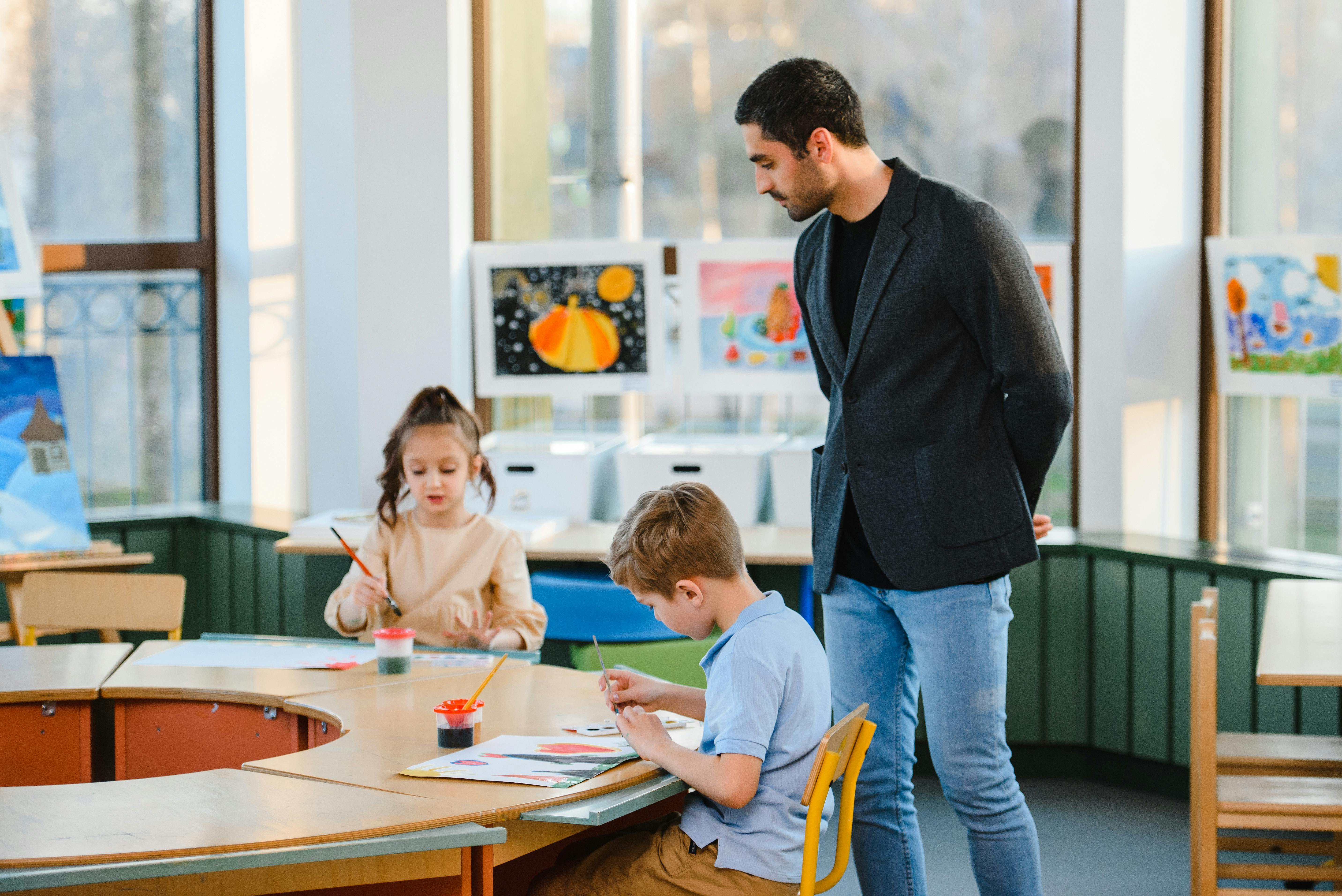 Genç öğrenciler sınıfta resim yaparken öğretmenleri onları izliyor