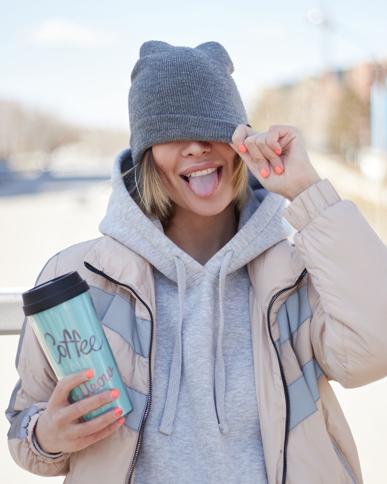 Young woman in a gray slouchy beanie pulled low over her eyes, holding a coffee cup