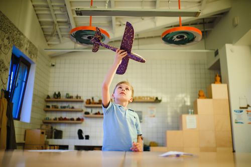 Free A young boy in a blue shirt plays with a toy plane indoors, reaching upward enthusiastically. Stock Photo