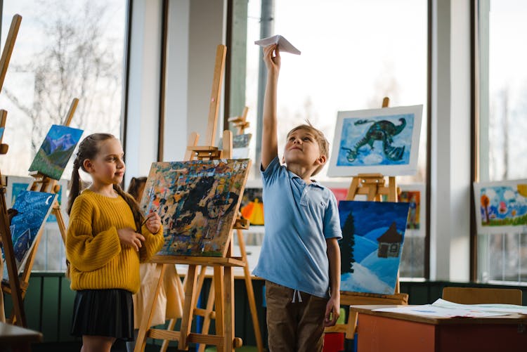 Girl In Yellow Sweater Watching A Boy Playing With Paper Plane