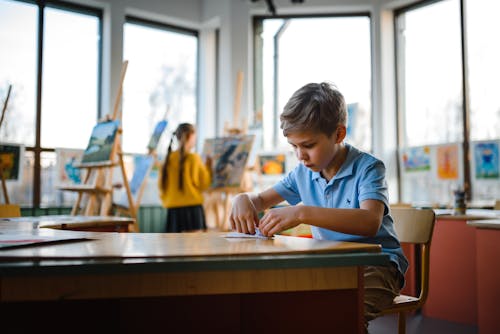 Boy in Blue Button Up Shirt Making A Paper Plane