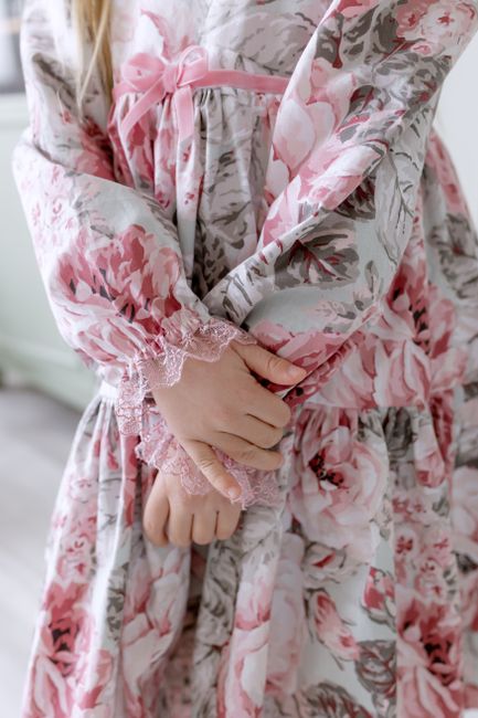 A close-up of a young girl's hands folded, wearing a pink floral pattern dress.