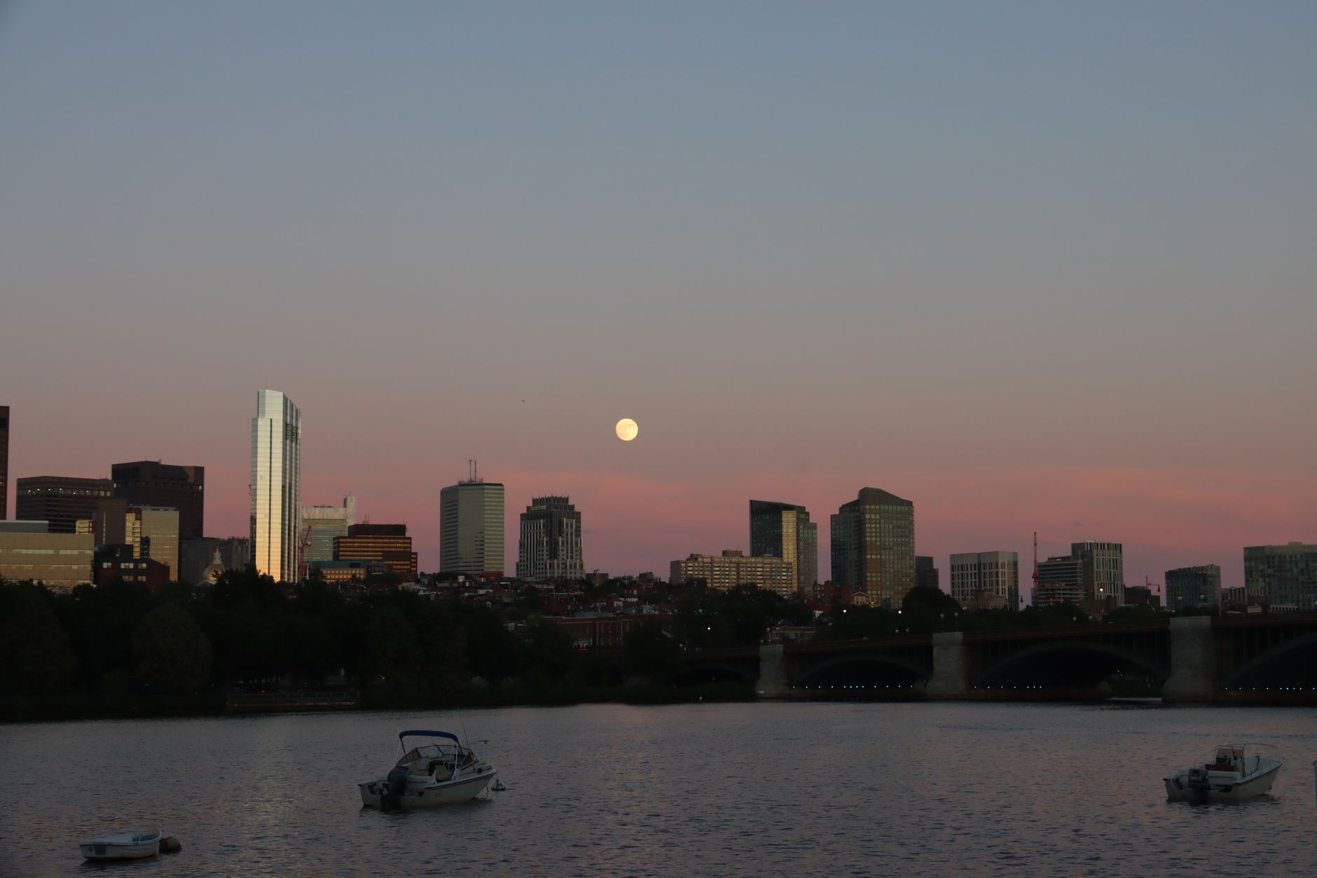 Scenic view of Boston skyline and Charles River at dusk with a full moon backdrop.