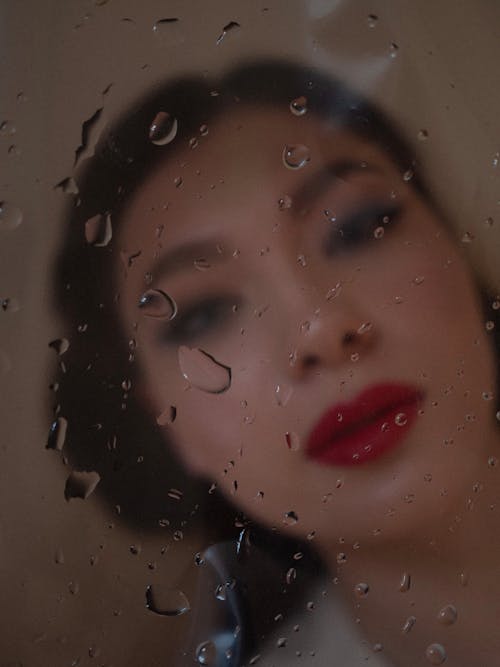 Blurry Image of Woman over a Glass with Drops of Water