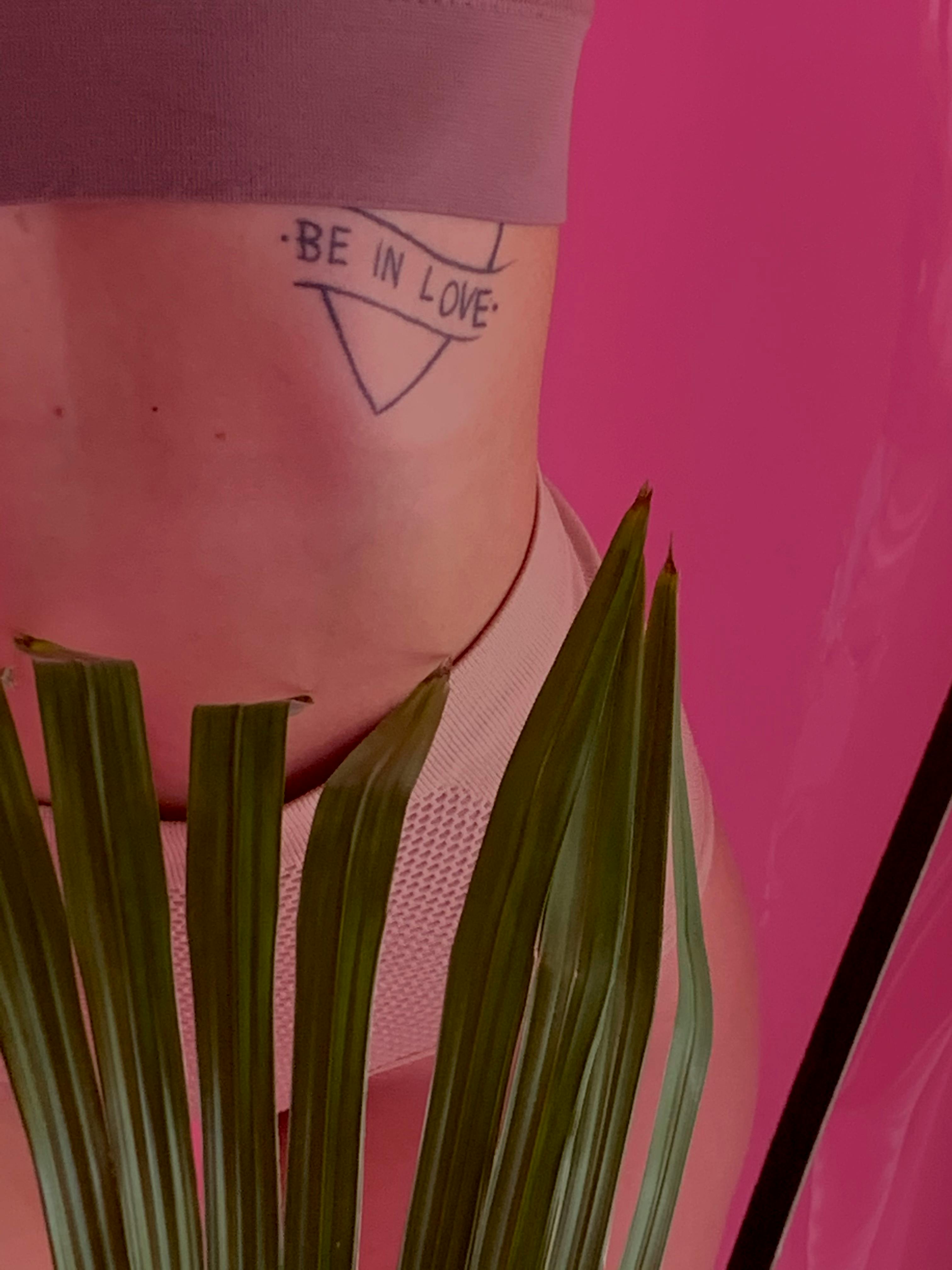 Artistic close-up of a tattooed body and palm leaves against a vibrant pink background.
