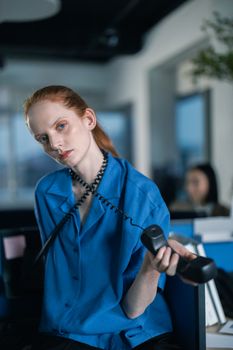 Thoughtful woman holding telephone in a modern office, staring intently.