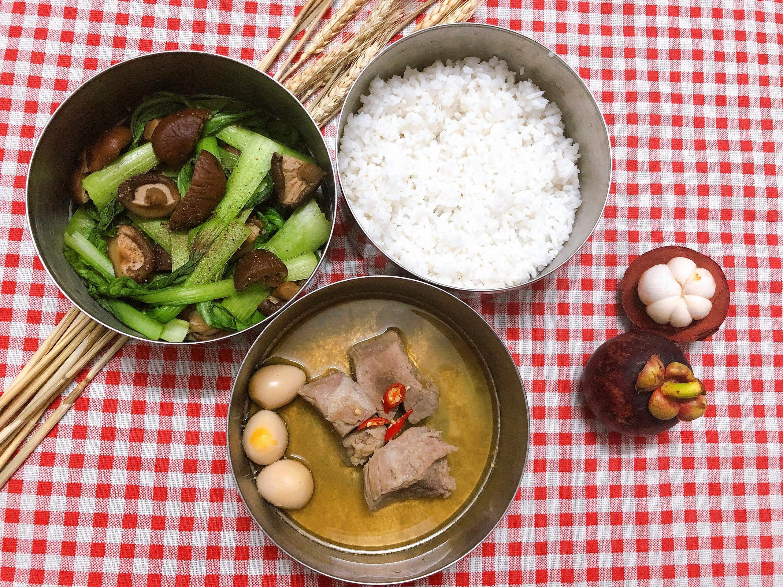 Flat lay of a traditional Vietnamese meal with rice, vegetables, and meat on a red checkered cloth.