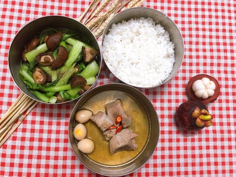 Flat lay of a traditional Vietnamese meal with rice, vegetables, and meat on a red checkered cloth.