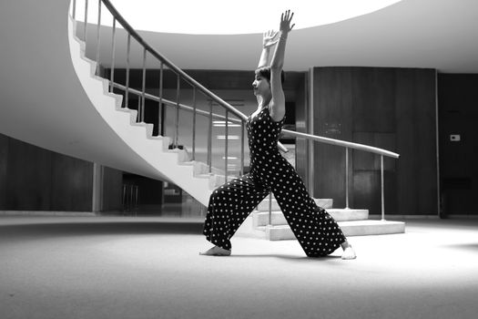 Black and white photo of a woman in a yoga pose by spiral staircase indoors.