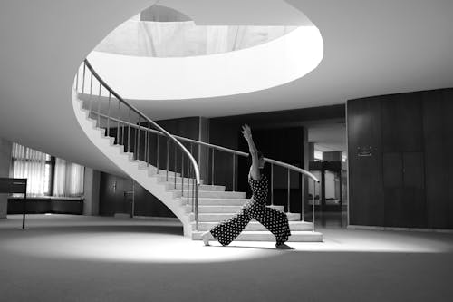 Grayscale of a Woman in Polka Dots Jumpsuit Doing Yoga Pose Beside the Staircase