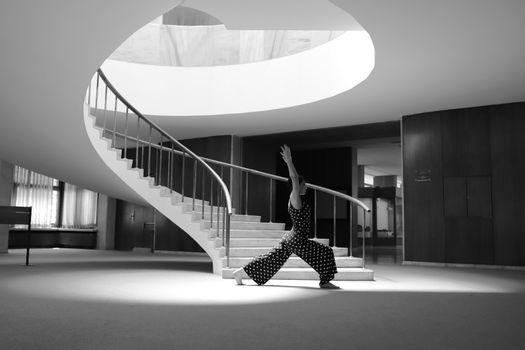 A woman performs a yoga pose on a minimalist, spiral staircase, captured in black and white.
