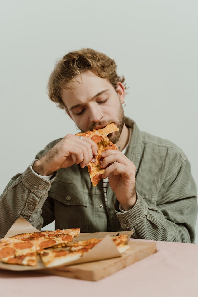 Man In Green Jacket Eating Pizza With Eyes Closed