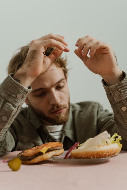 Free A bearded man in casual attire is looking at a deconstructed hamburger on a table. Stock Photo