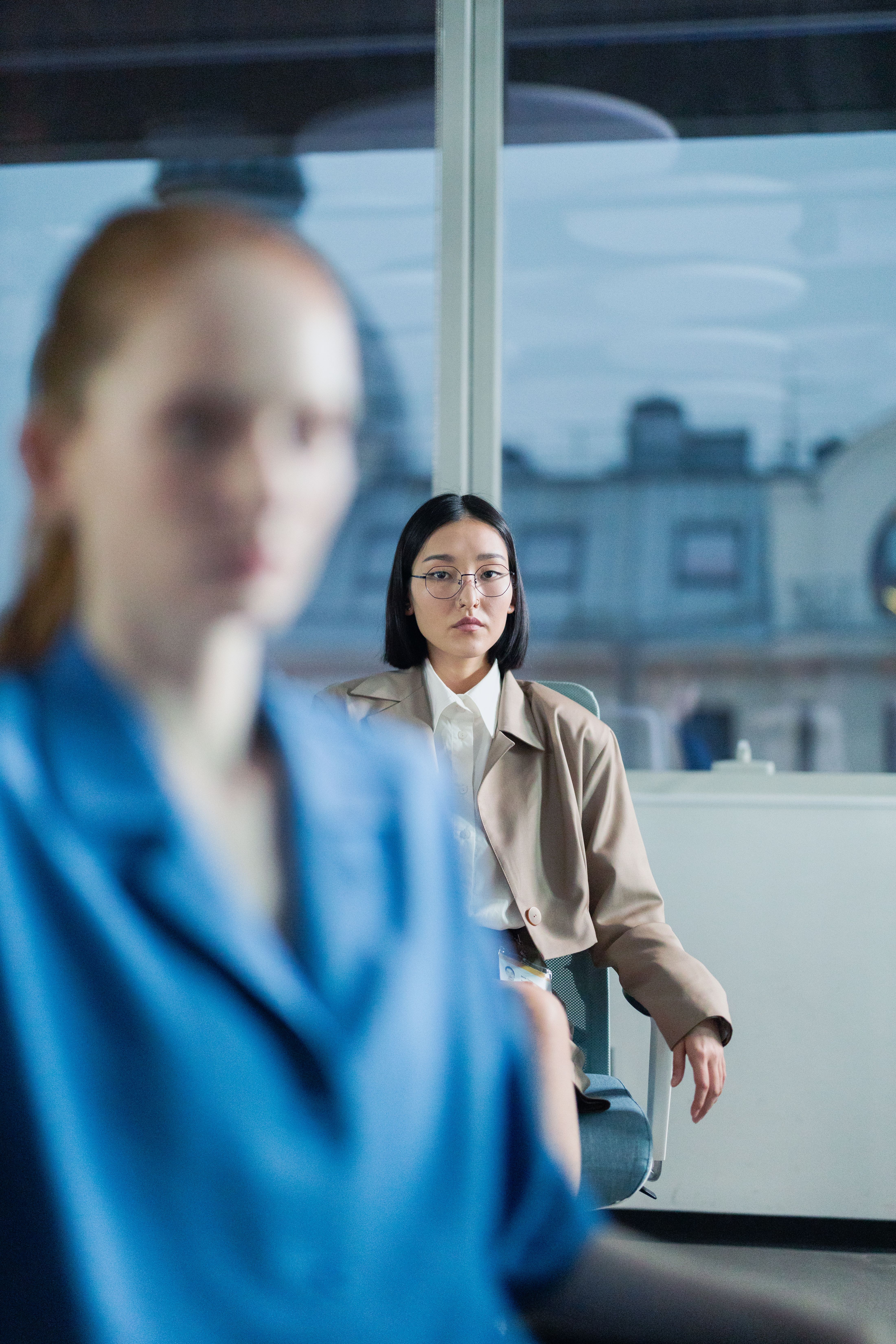 Focused woman sitting in a modern office setting with city view, conveying professionalism.