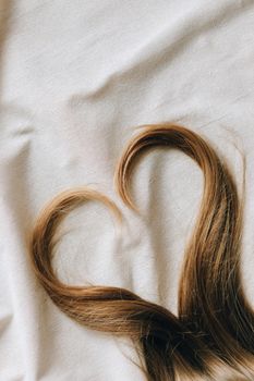 Close-up of brown hair arranged in a heart shape on soft white fabric. Perfect for love-themed designs.