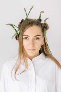 A woman with asparagus styled in her hair, wearing a white blouse against a white background.