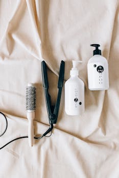 Flat lay of hairbrush, hair iron, and shampoo bottles on fabric background.