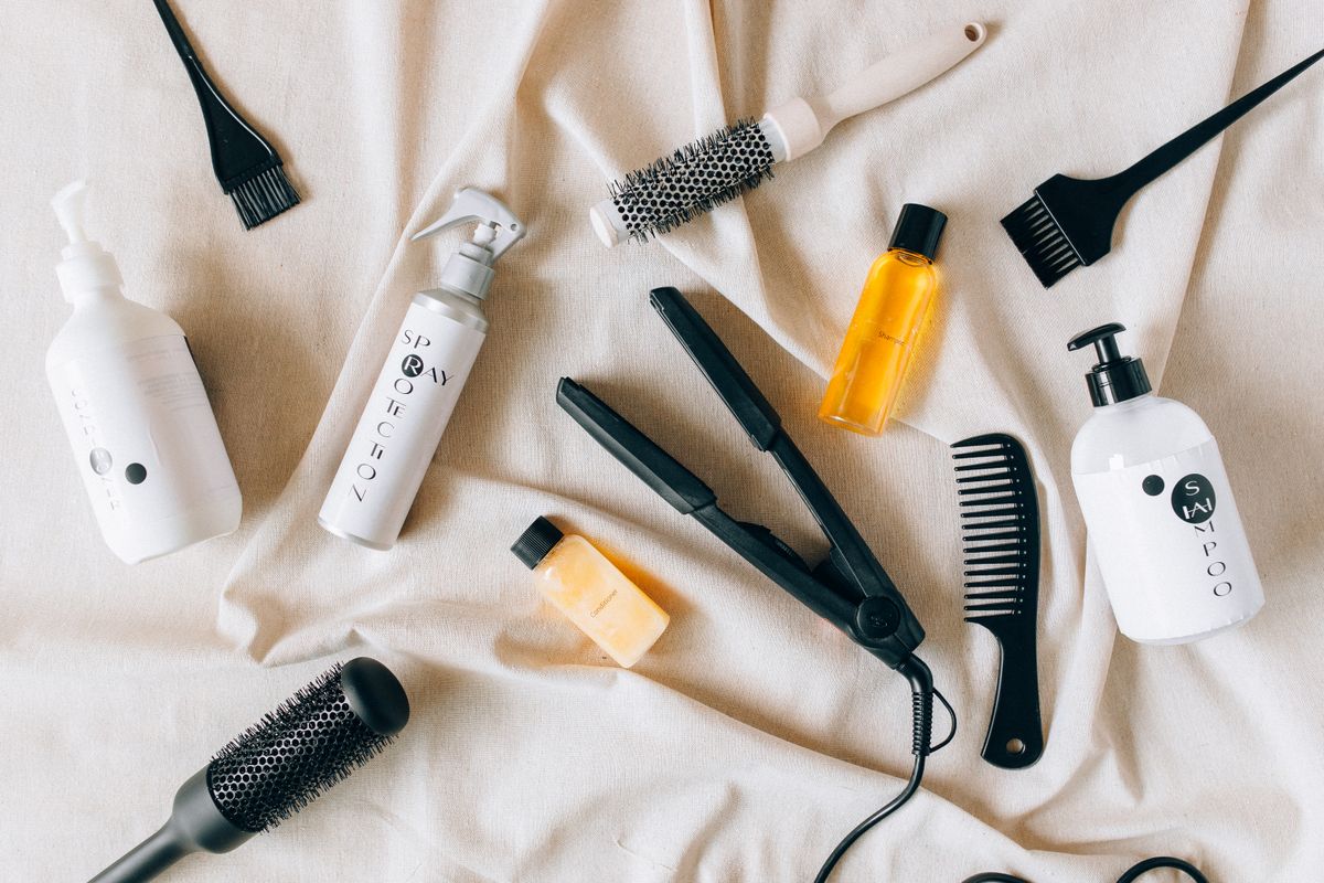 Flat lay of hair care products including shampoo bottles, brushes, and treatment oils on fabric