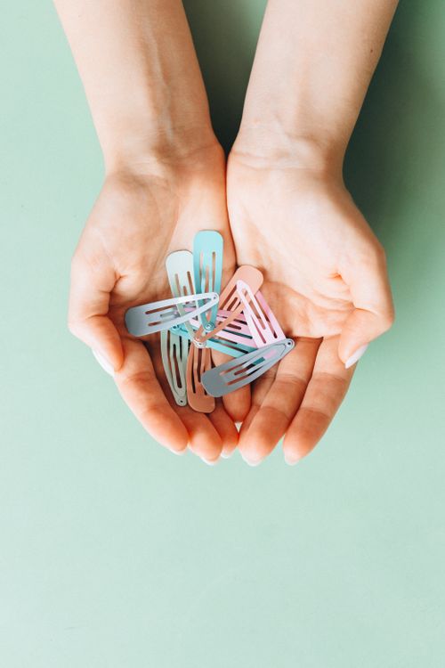Free Close-up of hands holding pastel colored hair clips on a mint green background. Stock Photo