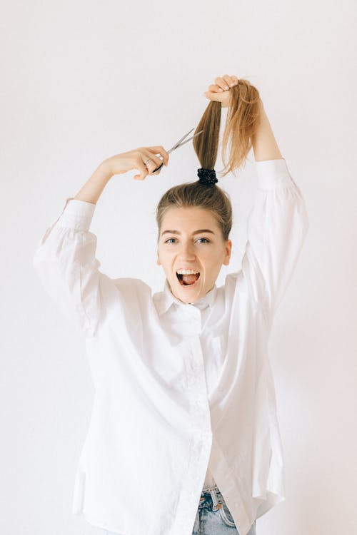 A Woman in White Long Sleeves Cutting Her Hair