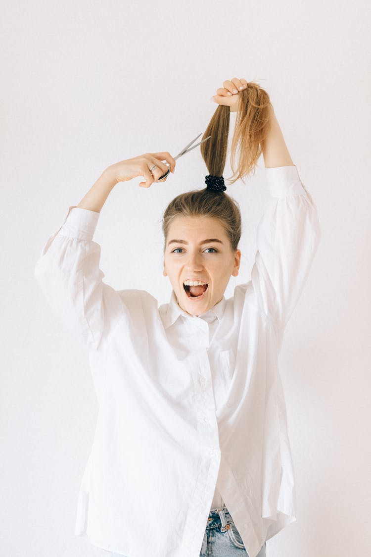 A Woman In White Long Sleeves Cutting Her Hair