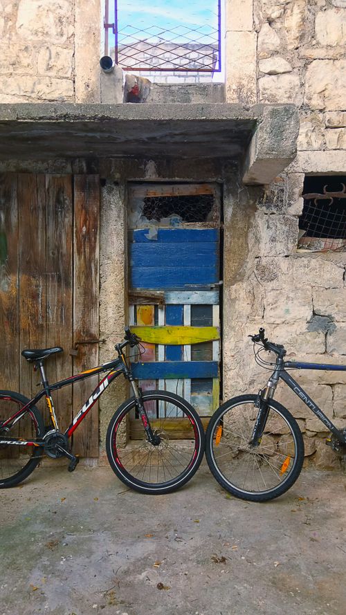 Free Two bicycles leaning against an old, rustic building facade with wooden doors. Stock Photo