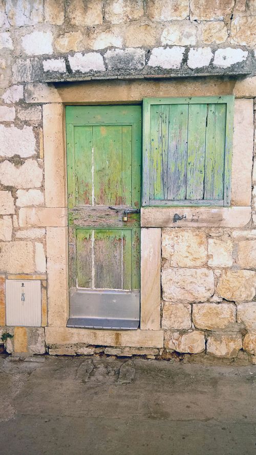 Free A vintage green wooden door with weathered texture in a rustic stone facade. Stock Photo