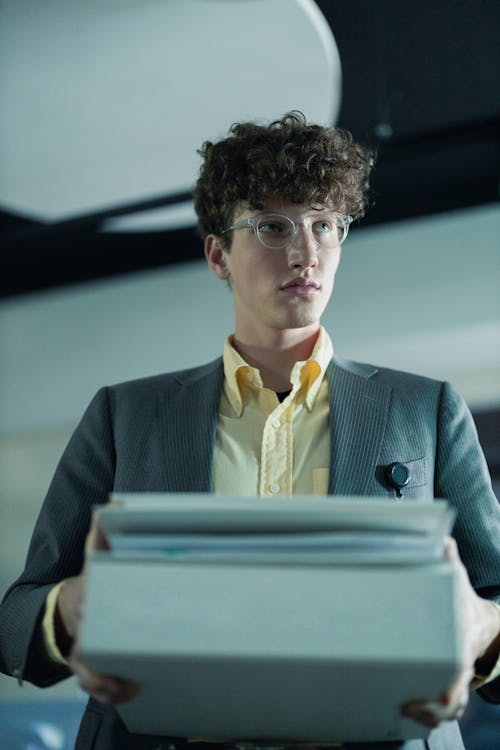 Man in Elegant Gray Blazer and Yellow Shirt Carrying a Stack of Documents