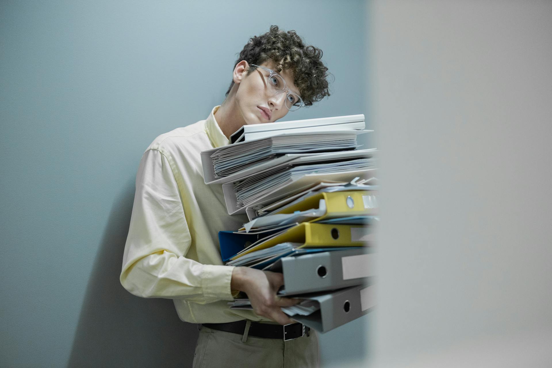 Young man overwhelmed with a stack of folders symbolizes workplace stress.