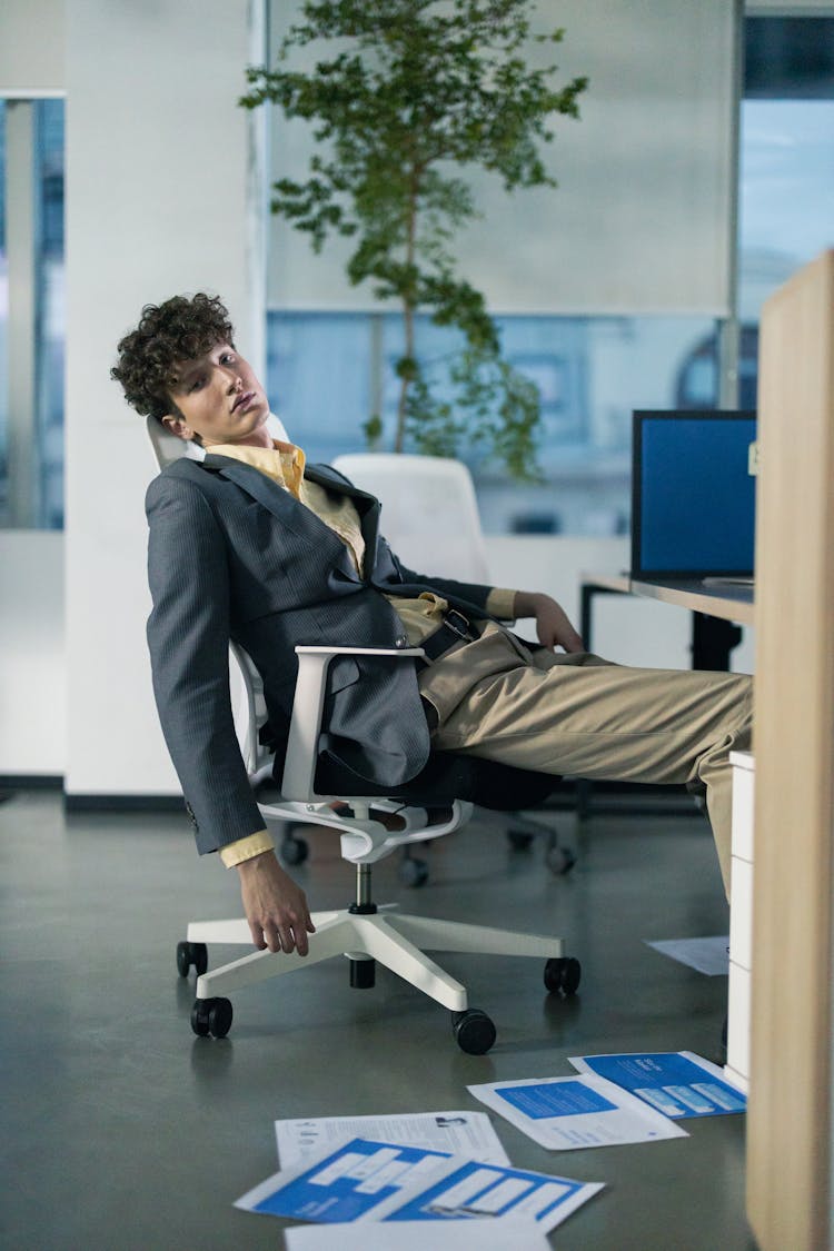 Man In Black Suit Jacket Sitting In An Office Chair Feeling Tired