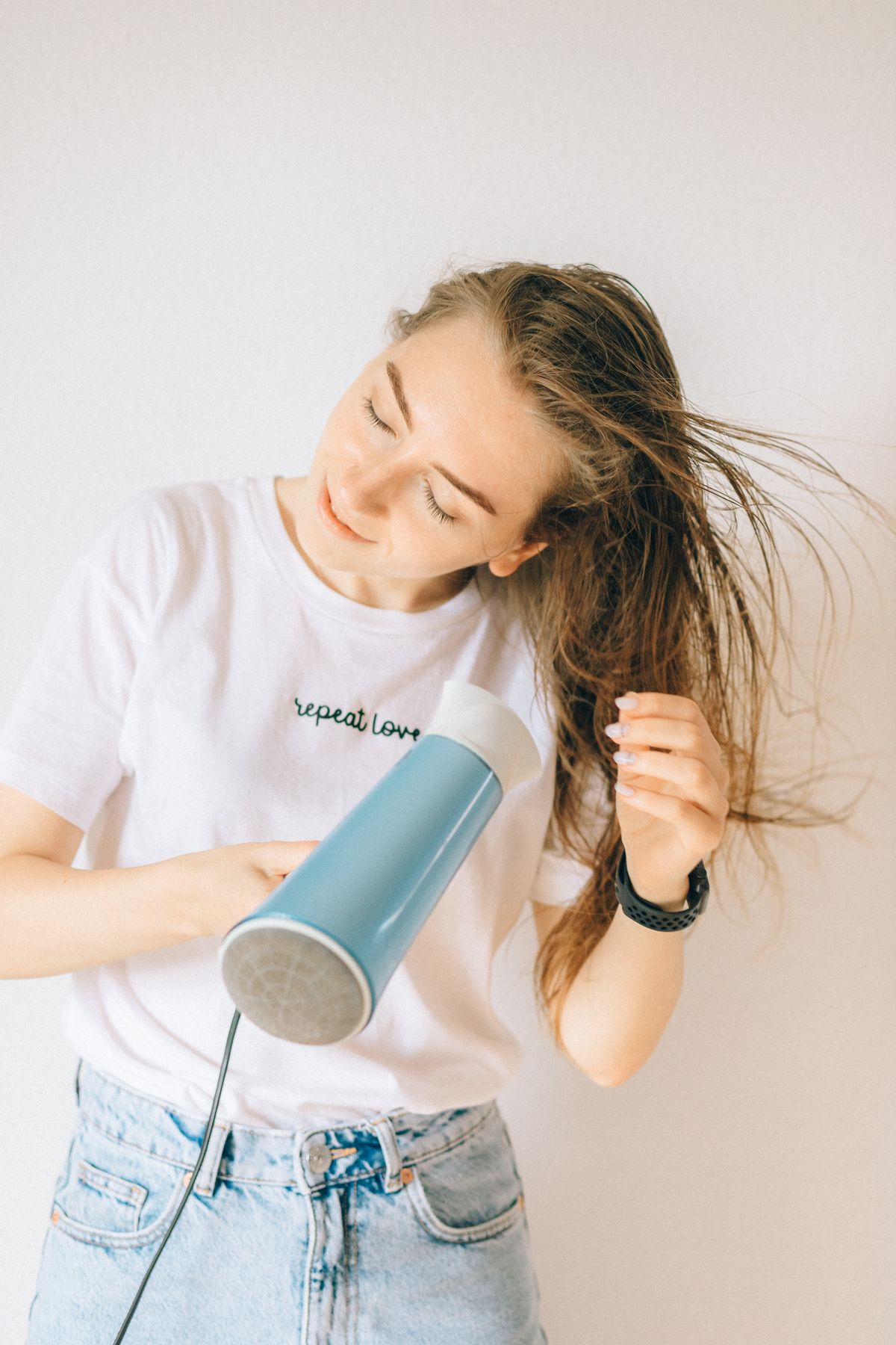 A young woman using a hair dryer to dry her long brown hair indoors