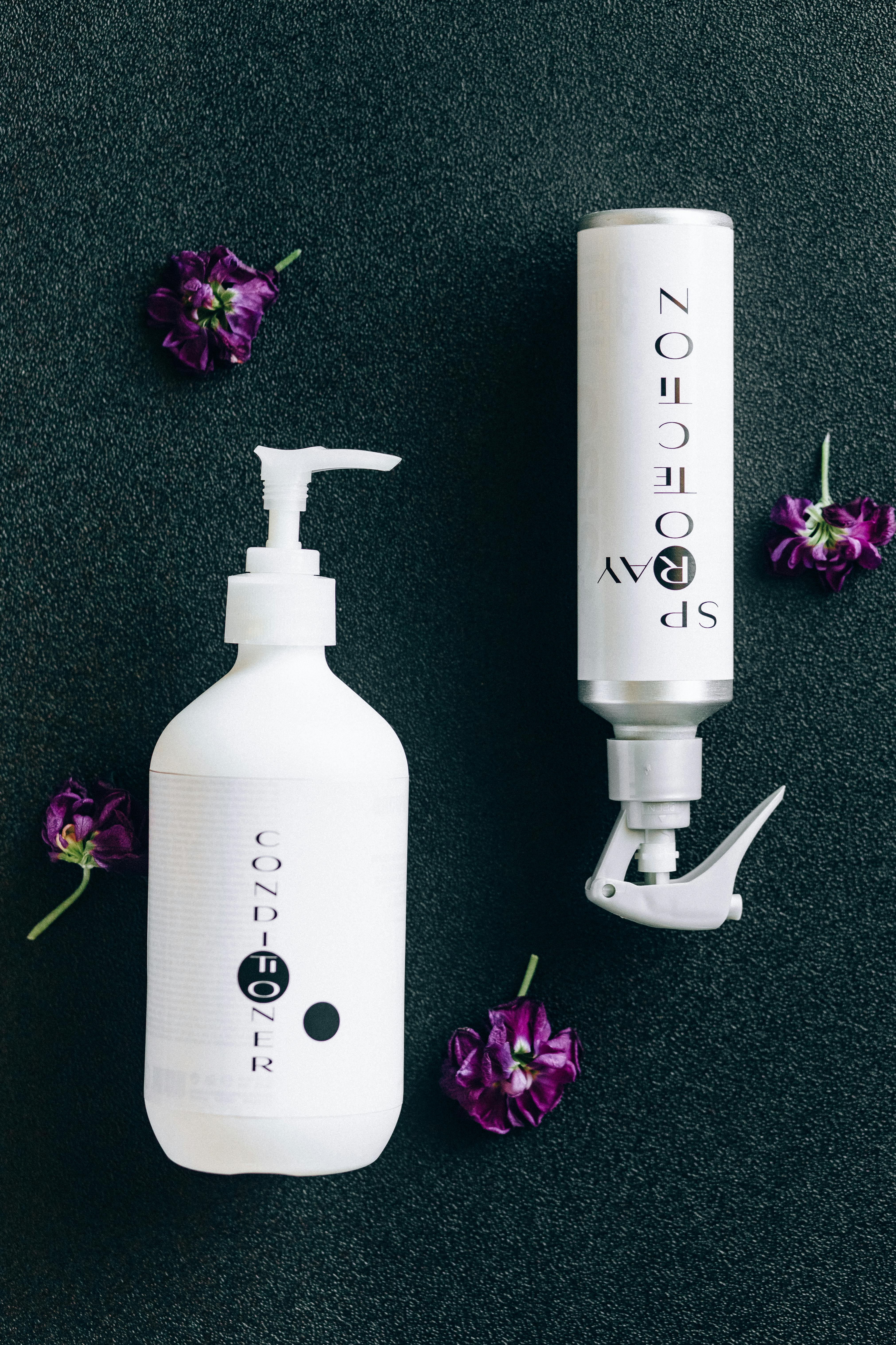 Styled product flat lay featuring conditioner and spray bottles with purple flowers.