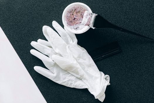 Flat lay of hairdressing tools including dye brush, latex gloves, hair dye bowl, and comb.