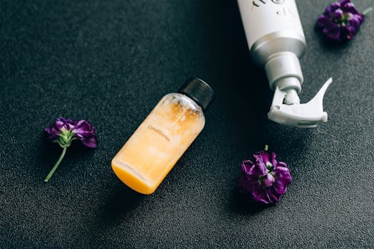 Elegant flat lay of conditioner and spray bottle with vibrant purple flowers on dark background.
