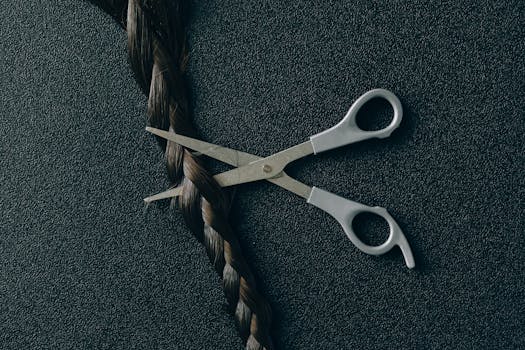 Artistic display of scissors poised to cut a braid against a dark textured backdrop.