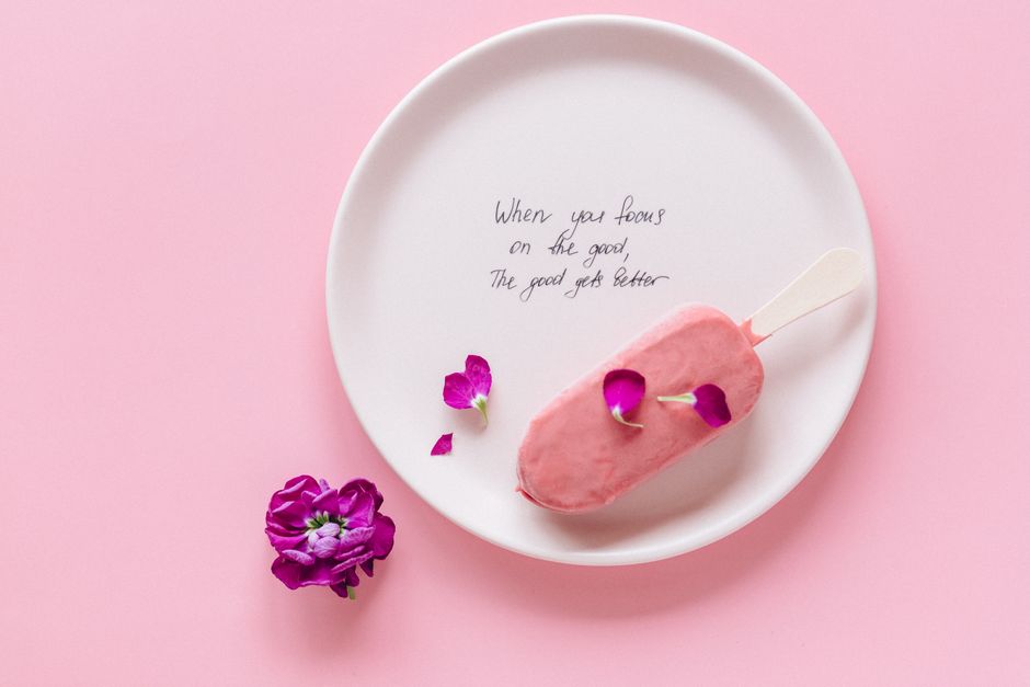 Flat lay of pink ice cream with petals and uplifting quote on plate.
