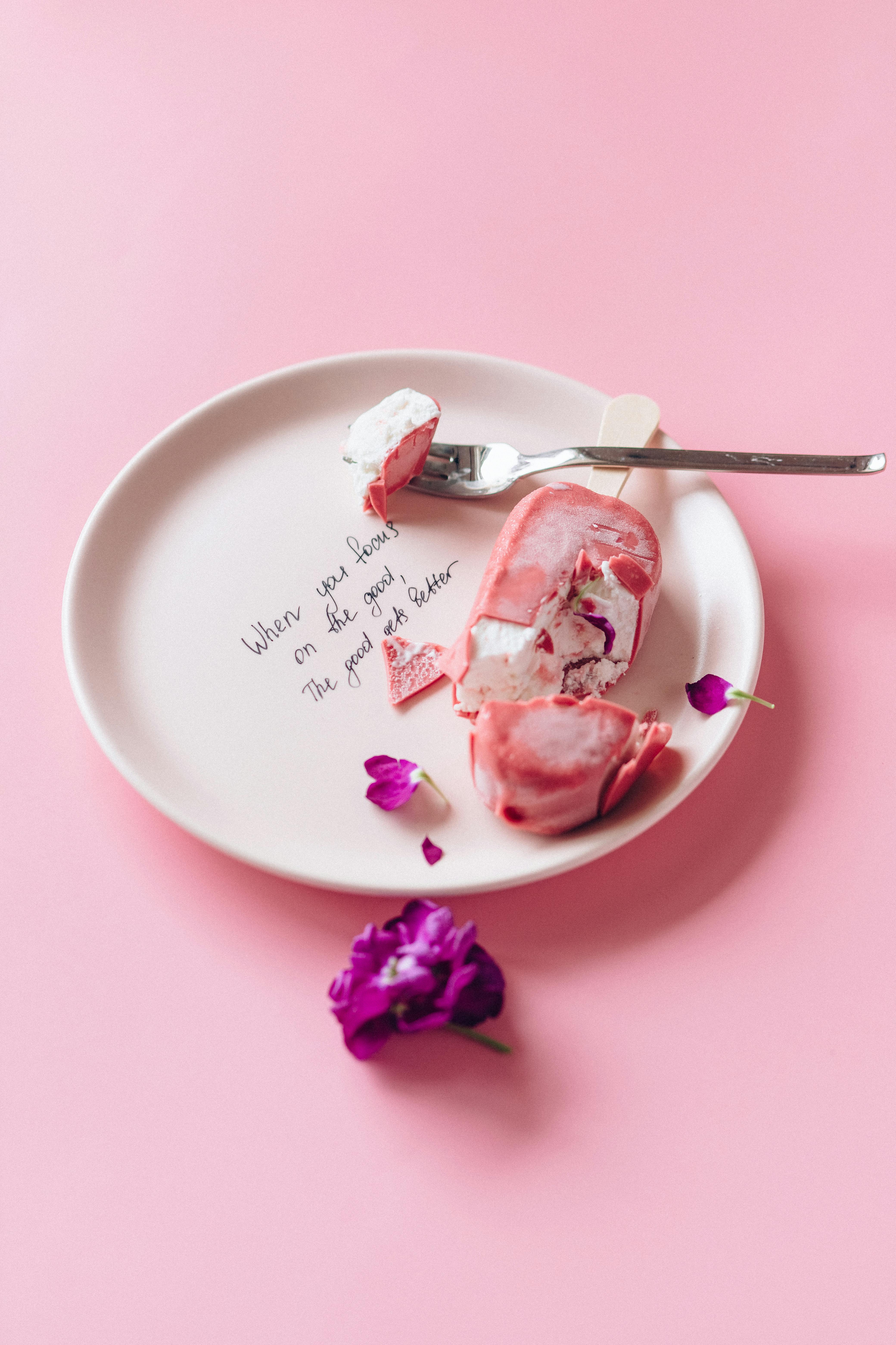 Delicious ice cream dessert served on a plate with pink background and a purple flower.