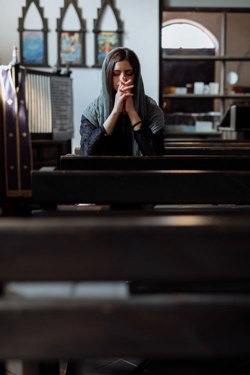 Free A woman meditates in a church, eyes closed and hands clasped, in peaceful reflection. Stock Photo