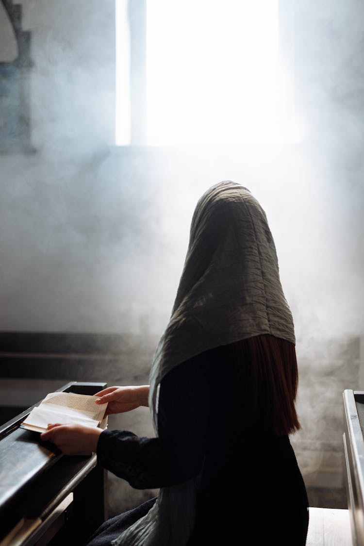 A Woman With Veil Holding A Book While Looking At The Window