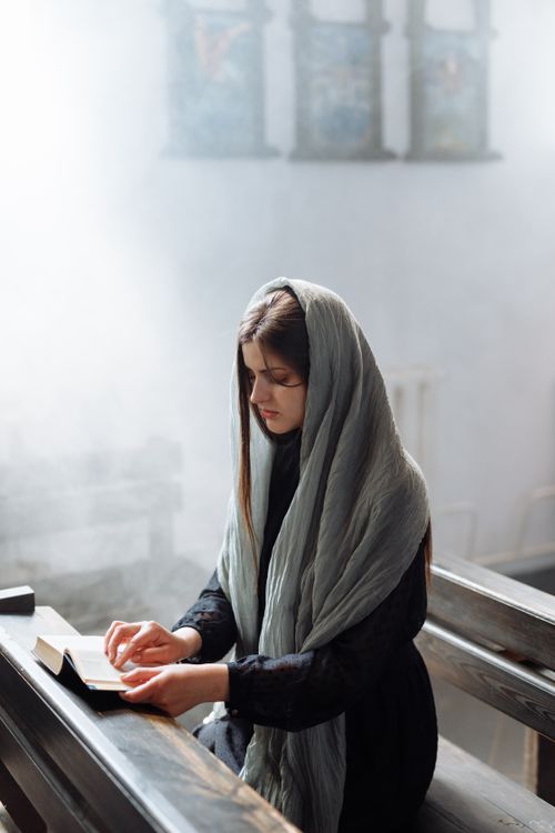 Free A young woman in a headscarf reads a bible inside a church, bathed in soft natural light. Stock Photo