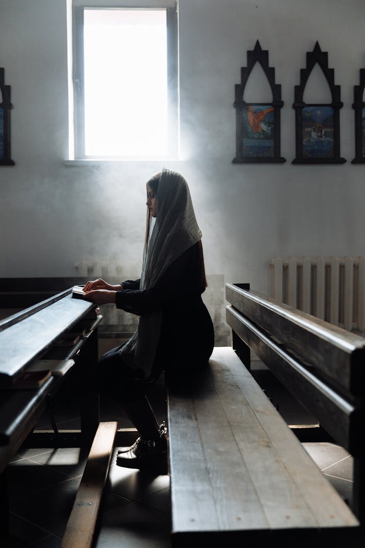 Woman In Black With Scarf On Head Sitting On Bench In Church