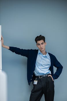 A young professional man posing confidently in smart attire against a neutral background.