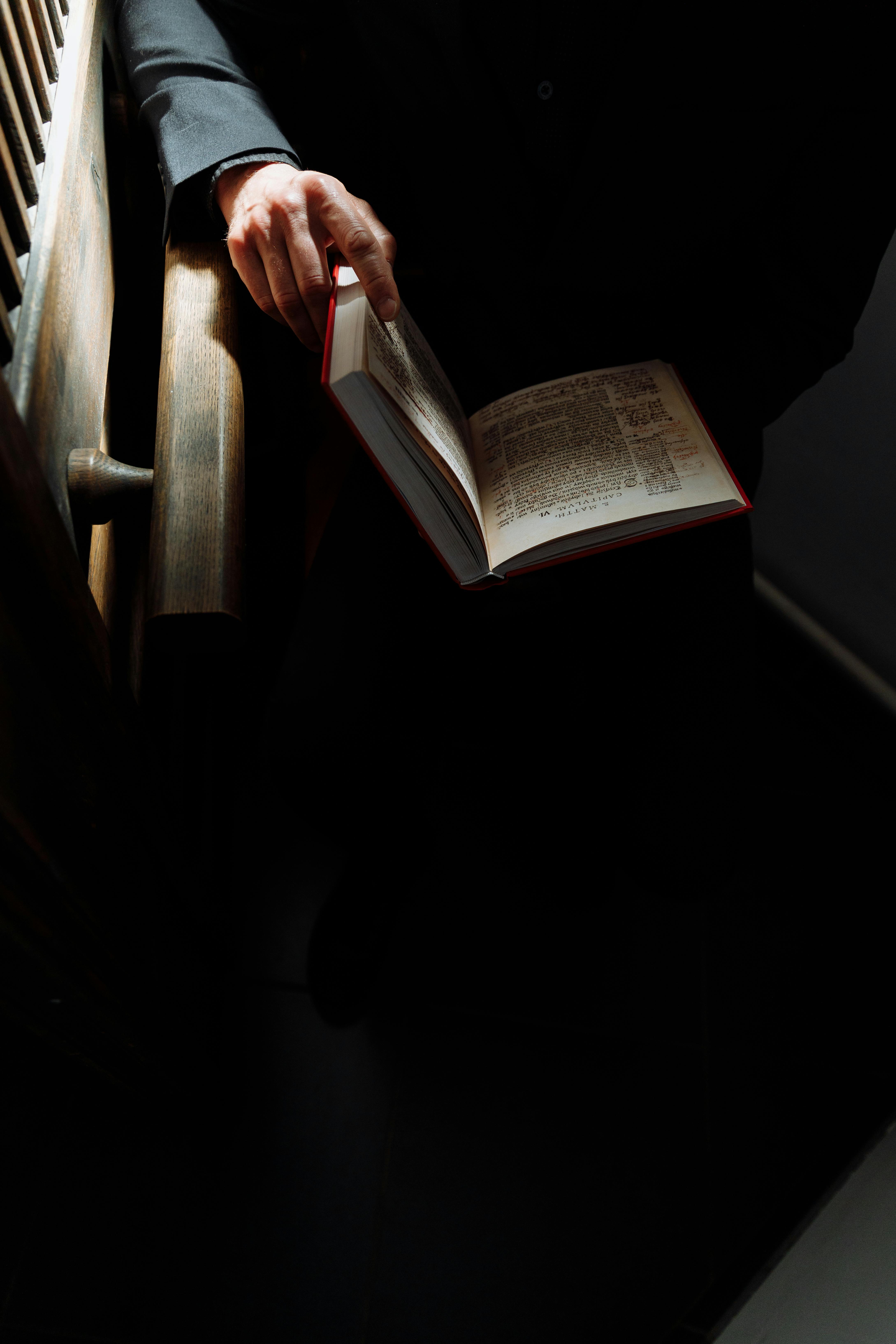 Free Sunlit scene of a man holding and reading a book indoors, with strong contrast and shadows. Stock Photo