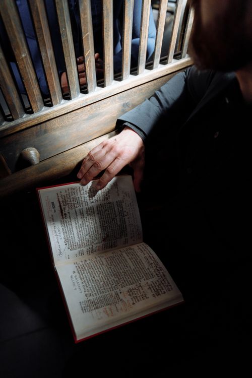 Free A close-up of a person reading a prayer book in a traditional confessional setting, capturing a moment of spirituality. Stock Photo