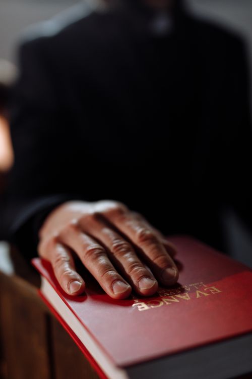 Free Close-up of a hand resting on a red religious book, emphasizing faith and spirituality. Stock Photo