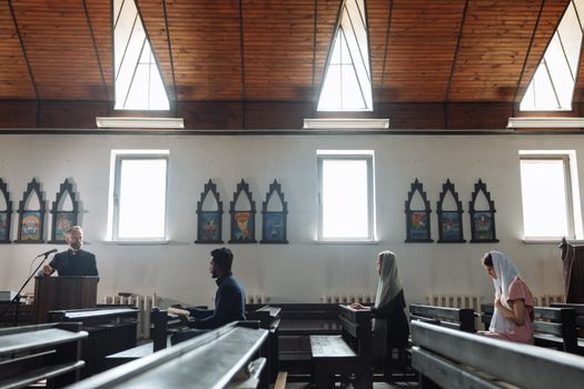 A serene church interior with people praying and a priest presiding from a pulpit.