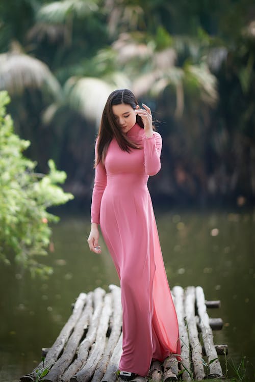 Woman in a Pink Maxi Dress Standing on a Small Pier 