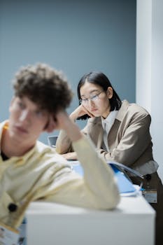 Two office colleagues sitting thoughtfully at desks, focused and serious.
