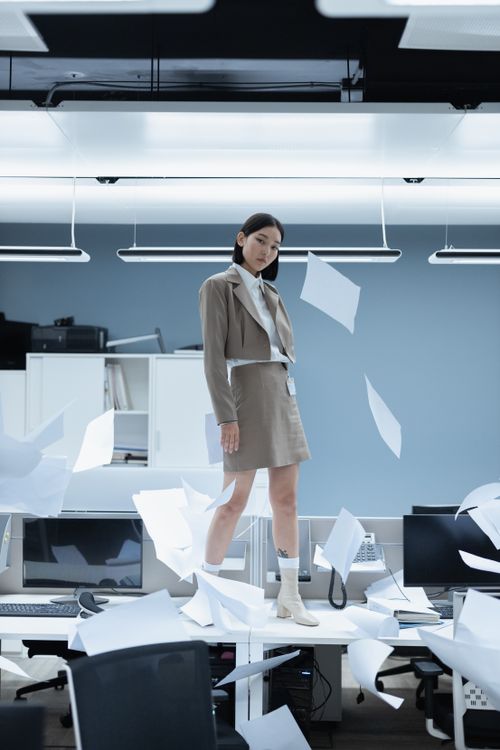 Free An overworked woman in an office stands amid flying papers, expressing stress and chaos. Stock Photo