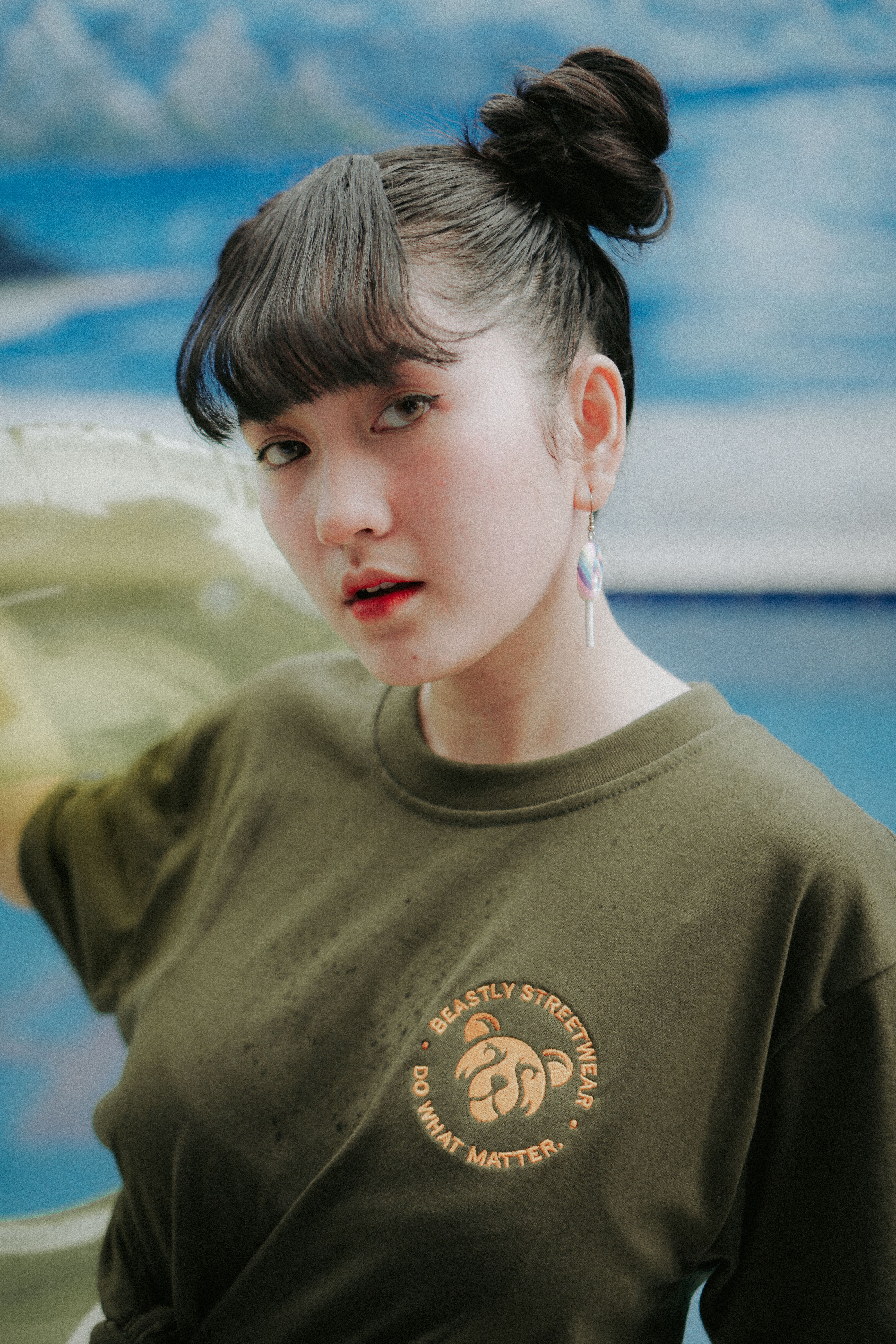 Trendy young Asian woman in stylish casual wear posing outdoors against a vibrant backdrop.